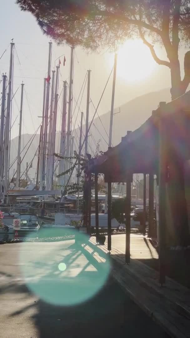 Türkei, Fethiye, 06. Oktober 2021: Yachthafen mit vielen Segelbooten bei Sonnenaufgang, vielen Masten, eine ältere Frau auf dem Fahrrad, Pier, sonniges Wetter, Berge am Horizont — Stockvideo