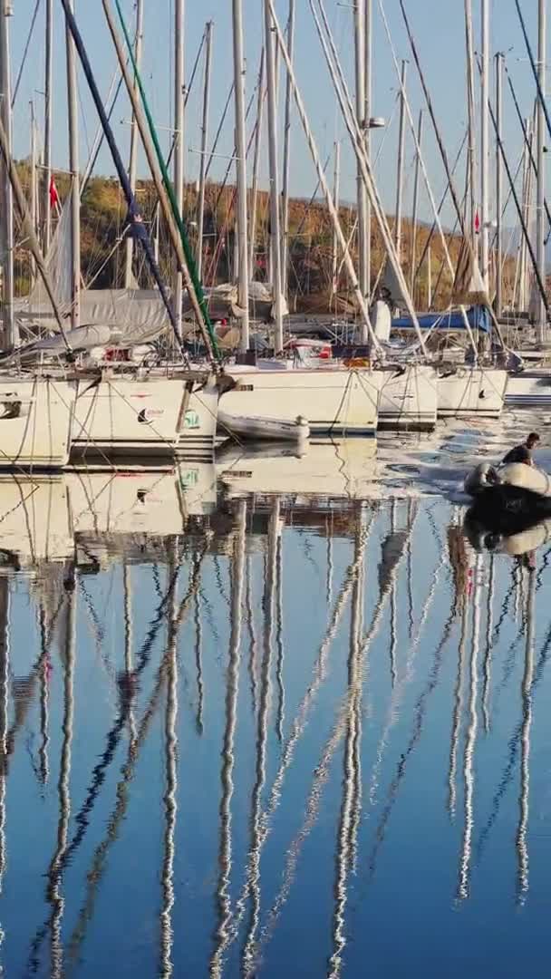 Turquia, Fethiye, 06 de outubro de 2021: As imagens verticais da marina com muitos veleiros pela manhã, muitos mastros, espelhando em águas calmas em tempo ensolarado, assistente de barco, montanhas no horizonte — Vídeo de Stock