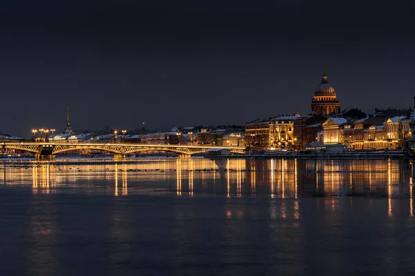 Панорамні кадри зимового нічного міста Санкт-Петербург з мальовничим відображенням на воді, кафедральний собор Ісаака на задньому плані, Благороський міст, стара назва - лейтенант Шмідт. Стокове Фото