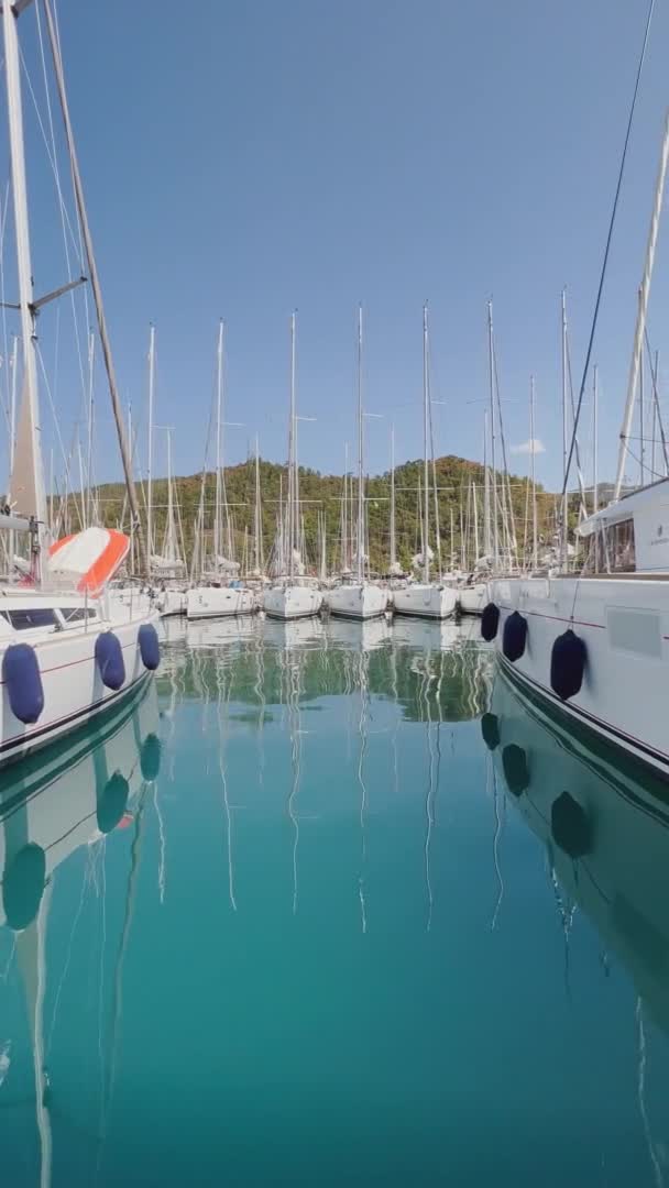 Turkey, Marmaris, 02 October 2021: The vertical footage of marina with many sailboats in the morning, many masts, mirroring on calm water in sunny weather, mountains on the horizon — Stock Video