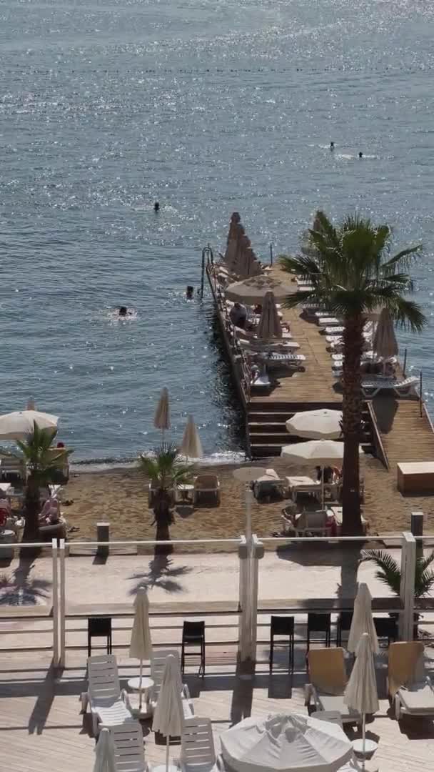 Turquía, Marmaris, 02 de octubre de 2021: Muelle con tumbonas en el paseo marítimo del complejo vacacional, la gente tomando el sol pasa las vacaciones durante la pandemia, la playa de arena y las palmeras en tiempo soleado — Vídeos de Stock