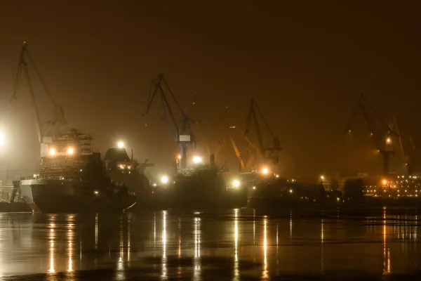 The construction of nuclear icebreakers at night, cranes of of the Baltic shipyard in a frosty winter day, steam over the Neva river, smooth surface of the river, fog — Stock Photo, Image