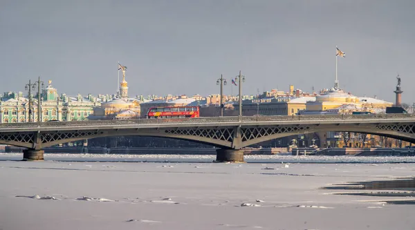 Der Blick auf die Winterstadt Sankt-Petersburg, den zugefrorenen Fluss Newa, den roten Touristenbus auf der Blagoweschtschenko-Brücke, den Winterpalast, das Admiralsgebäude, die Alexander-Säule im Hintergrund — Stockfoto