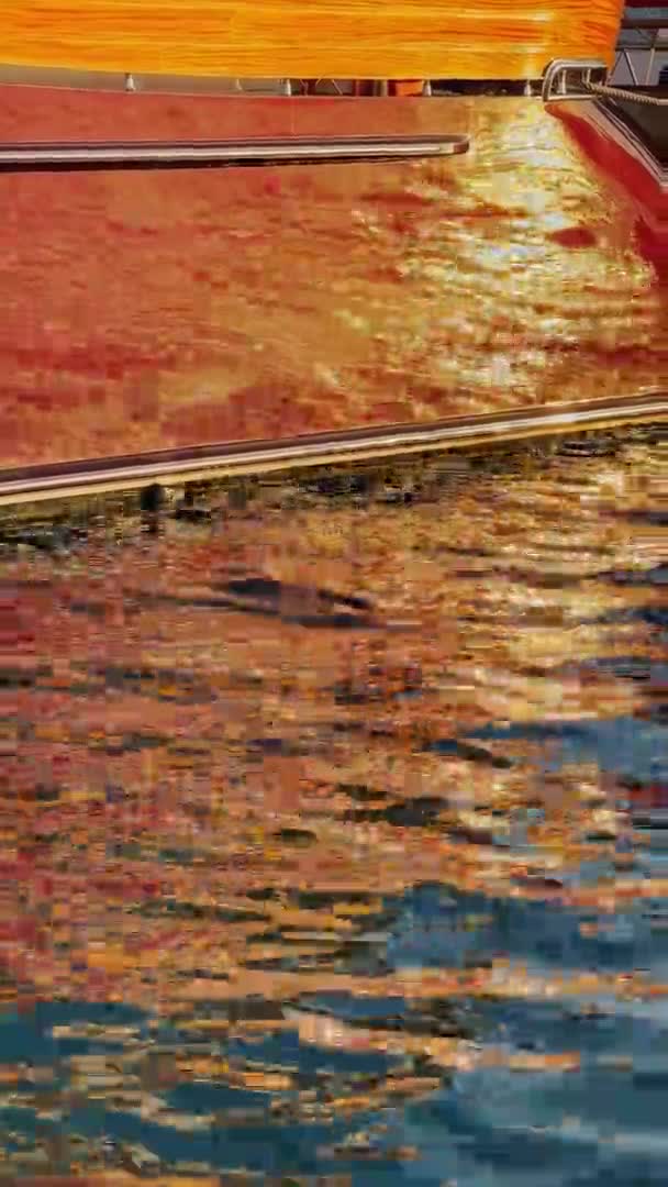 Verticale beelden van de kleurrijke reflectie van boord van enorme boot op het water, kleine golven, blauw water in slow motion — Stockvideo