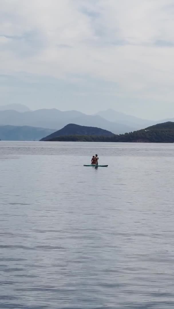 Turkije, Sarsala, 03 oktober 2021: De pittoreske baai van Sarsala eiland in de avond, mensen drijven op sup of paddle board in de buurt van eiland, in de buurt van Marmaris, bergen op de achtergrond — Stockvideo