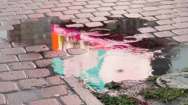 Reflet couleur de l'écran publicitaire dans une flaque d'eau sous la pluie, vidéo floue abstraite, silhouettes de passants — Video