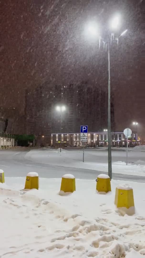 Arado de nieve tractor elimina la nieve de la carretera en el estacionamiento cerca de gran tienda centro comercial lote, mientras que no hay coches por la noche, iluminación nocturna, caída de nieve, centro comercial, ventisca de nieve — Vídeo de stock