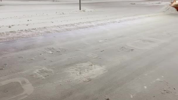 Traktor bajak salju memindahkan salju dari jalan di tempat parkir sementara tidak ada mobil di malam hari, pencahayaan malam, salju turun — Stok Video