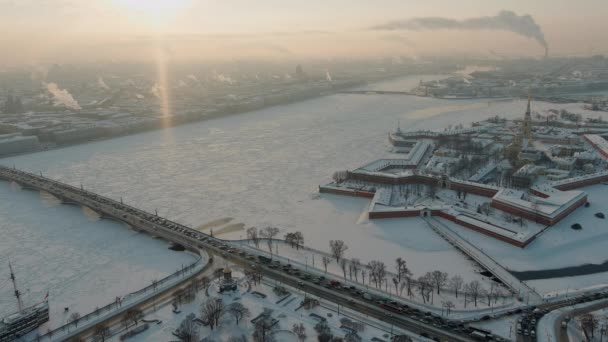 Съемка с беспилотника зимнего пейзажа Санкт-Петербурга на закате, замерзшая река Нева, пар над городом, Петропавловская крепость, автомобильное движение на Троицком мосту, ростральные колонны, Дворцовый мост, панорамный вид — стоковое видео