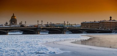 Gün batımında St. Petersburg 'un panoramik manzarası, arka planda Isaac Katedrali ve Blagoveshenskiy köprüsü, donmuş Neva nehri üzerinde buhar, turuncu renkli gökyüzü