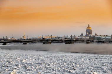 Gün batımında St. Petersburg 'un panoramik manzarası, arka planda Isaac Katedrali ve Blagoveshenskiy köprüsü, donmuş Neva nehri üzerinde buhar, turuncu renkli gökyüzü