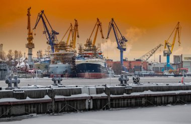 Nükleer buz kırıcıların sihirli günbatımında inşası, soğuk bir kış gününde Baltık tersanesinin vinçleri Neva nehrinin üzerinde buhar, nehrin pürüzsüz yüzeyi, turuncu renkli gökyüzü.
