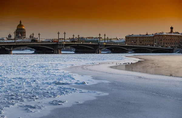 Gün batımında St. Petersburg 'un panoramik manzarası, arka planda Isaac Katedrali ve Blagoveshenskiy köprüsü, donmuş Neva nehri üzerinde buhar, turuncu renkli gökyüzü