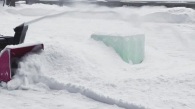Kar temizleme makinesi kullanan bir adam bahçedeki karları temizliyor.