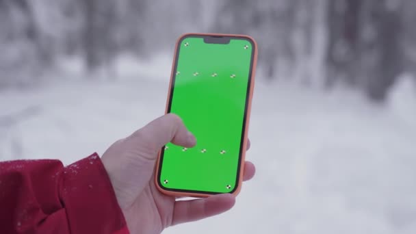 Smartphone di tangan seorang pria, hutan bersalju di latar belakang, jari bergerak pada layar hijau telepon, jari memindahkan layar ke kanan, seorang pria tersesat dan sedang mencari jalan — Stok Video