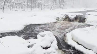 The wild frozen small river in the winter wood, the wild nature at snow storm, the river of red color, ice, snow-covered trees