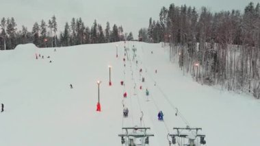 Drone view on cable way in ski resort. Ski lift elevator transporting skiers and snowboarders on snowy winter slope at mountain at weekend, drone flying over snowy slope