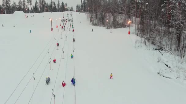 Drone view on cable way in ski resort. Ski lift elevator transporting skiers and snowboarders on snowy winter slope at mountain at weekend, drone flying over snowy slope — Wideo stockowe