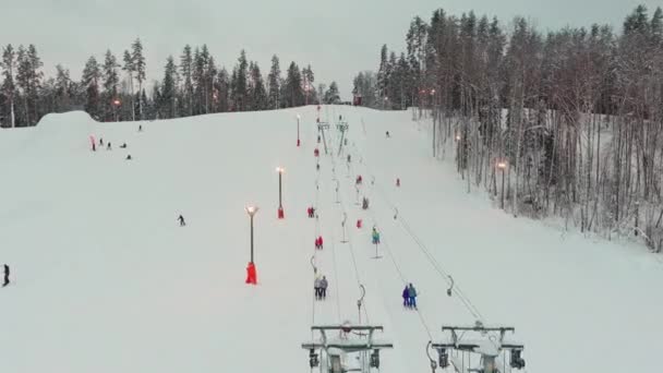スキー場でのケーブルウェイのドローンビュー。スキーリフト週末の山の雪の冬の斜面にスキーヤーやスノーボーダーを運ぶエレベーター、雪の斜面を飛び越えるドローン — ストック動画