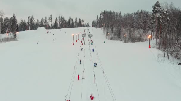 Drone view on cable way in ski resort. Ski lift elevator transporting skiers and snowboarders on snowy winter slope at mountain at weekend, drone flying over snowy slope — Stock Video