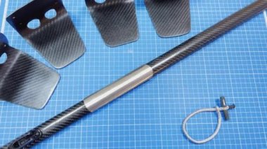 Several finished products made of carbon fiber lie on a blue table, a product in the form of a pipe with metal parts