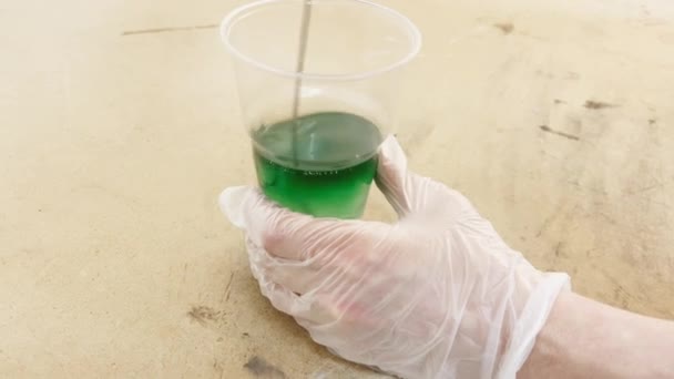 Gloved hands stir the green caustic liquid of green color in a plastic cup, industrial liquid for gluing carbon, the mixture interfere with the production mixer — Stock Video