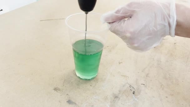 Gloved hands stir the green caustic liquid of green color in a plastic cup, industrial liquid for gluing carbon, the mixture interfere with the production mixer — Stock Video