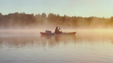 Russia, Karelia, 06 July 2021: Kayaker floats on calm water through the morning fog above the water at sunrise, the silhouette of a man with a paddle on a kayak, the golden color, magic light