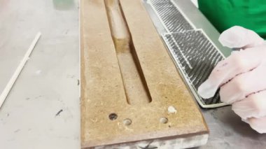 A specialist in protective gloves covers the baking form of a carbon product with a brush with industrial epoxy resin, strip of carbon fiber, mold for the press made of wood