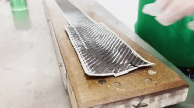 a specialist in protective gloves lays a layer of carbon cloth in a baking dish and cuts, strip of carbon fiber, mold for the press made of wood