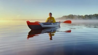 Russia, Karelia, 06 July 2021: Kayaker floats on calm water through the morning fog above the water at sunrise, the silhouette of a man with a paddle on a kayak, the golden color, magic light