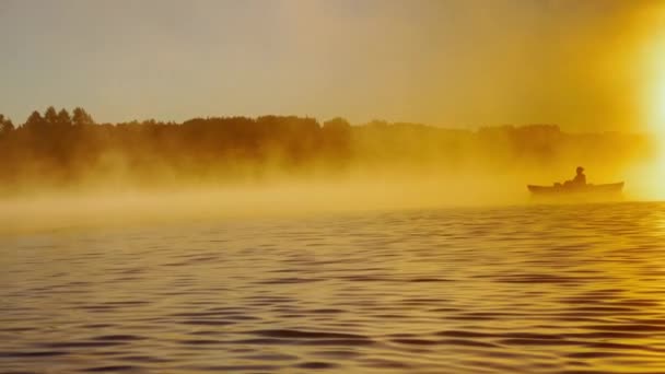 Kayaker floats on calm water through the morning fog above the water at sunrise, the silhouette of a man with a paddle on a kayak, the golden color of the water, warm water and cold air, magic light — Video Stock