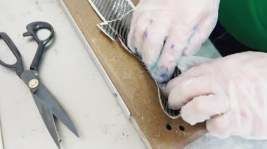 a specialist in protective gloves lays a layer of carbon cloth in a baking dish and cuts, strip of carbon fiber, mold for the press made of wood