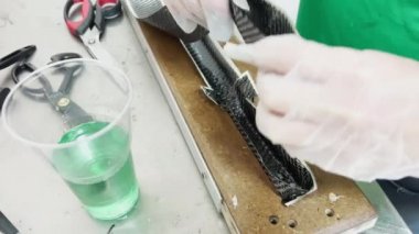 a specialist in protective gloves lays a layer of carbon cloth in a baking dish and cuts, strip of carbon fiber, mold for the press made of wood