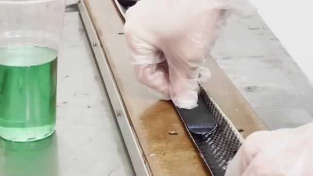 A specialist in protective gloves lays a layer of carbon cloth in a baking dish and cuts, strip of carbon fiber, mold for the press made of wood — Video