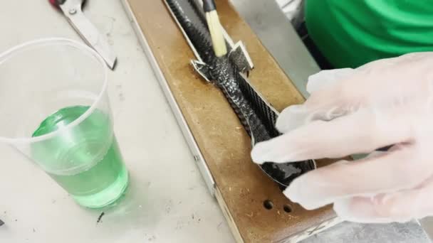 A specialist in protective gloves covers the baking form of a carbon product with a brush with industrial epoxy resin, strip of carbon fiber, mold for the press made of wood — Vídeo de Stock