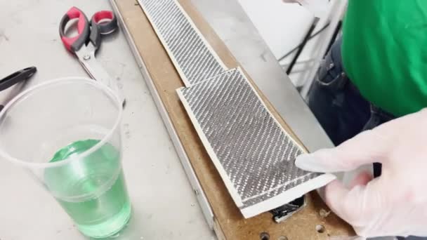 A specialist in protective gloves lays a layer of carbon cloth in a baking dish and cuts, strip of carbon fiber, mold for the press made of wood — Video