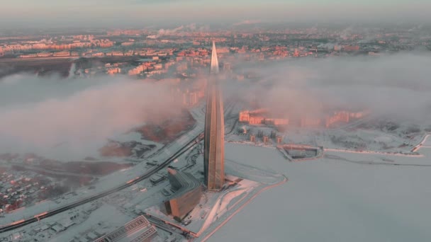 Россия, Санкт-Петербург, 08 января 2022 года: Небоскрёб Лахтинского центра в зимний морозный вечер на закате, будущее главное здание офиса нефтяной компании "Газпром", беспилотник летит к зданию — стоковое видео