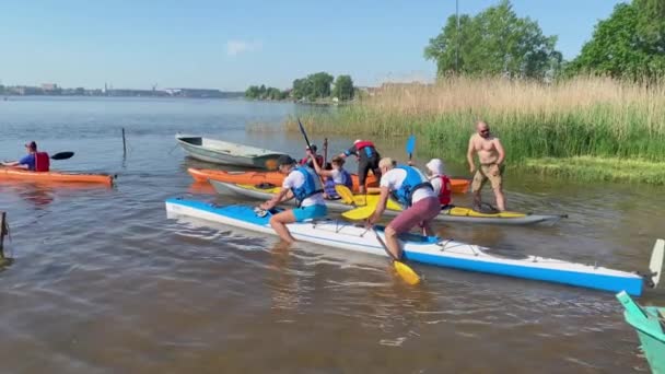 Rosja, Sankt Petersburg, 08 czerwca 2019: Ludzie przygotowują się do udziału w mistrzostwach wioślarskich miasta kajakarstwa, sportowcy przygotowują wiosła i kamizelki ratunkowe, wymaz filtrem przeciwsłonecznym, dzielą się doświadczeniami — Wideo stockowe