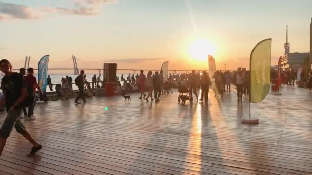 Russia, San Pietroburgo, 18 agosto 2019: La gente si rilassa sull'argine del complesso fieristico Sevkabel in una calda giornata estiva al tramonto, la gente balla, un cavo è rimasto ponte sullo sfondo — Video Stock