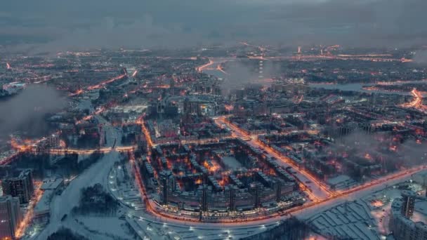 Letecká zimní městská krajina Petrohradu - Rusko, ve večerních hodinách přelety nad obrovskými sídlištěmi, stavební jeřáby, noční osvětlení, noční městská krajina, pod dronem se vznášejí mraky — Stock video