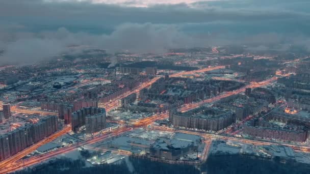 Paisaje urbano de invierno aéreo de San Petersburgo Rusia, el dron vuela sobre enormes propiedades habitacionales por la noche, grúas de construcción, iluminación nocturna, paisaje urbano nocturno, nubes flotan debajo del dron — Vídeos de Stock