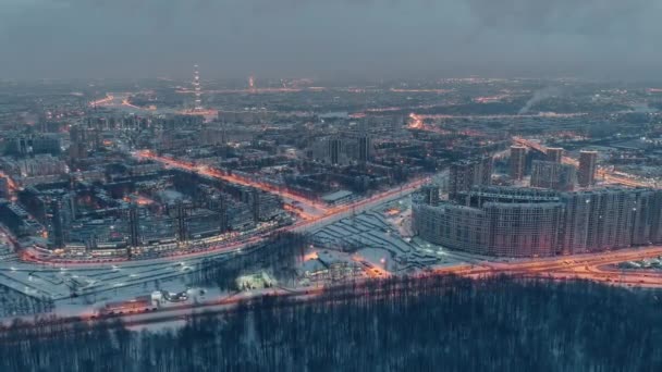 상트페테르부르크 공중에서 겨울을 나는 도시 경관 - 러시아, 저녁에는 드론 이 거대 한 주거 지역을 비행하고, 건축용 크레인, 야간 조명, 야간 도시 경관, 드론 아래로 구름이 떠다니고 있다 — 비디오