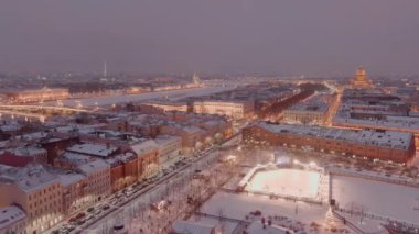 Karlı bir kış akşamında New Holland parkının hava manzarası, binaların ve sokakların gece aydınlanması, gece şehir manzarası, açık hava buz pateni pisti, arka planda St. Petersburg 'un simgeleri. 