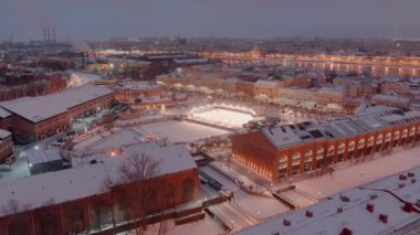 Karlı bir kış akşamında New Holland parkının hava manzarası, binaların ve sokakların gece aydınlanması, gece şehir manzarası, açık hava buz pateni pisti, arka planda St. Petersburg 'un simgeleri. 