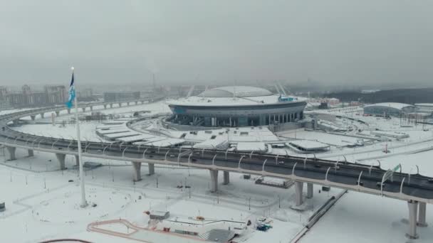 Ryssland, St Petersburg, 22 januari 2022: Drönaren flyger längs kabelbron mot den nya arenan Gazprom Arena i en snöstorm, flaggan av Zenit laget sveper på en enorm flaggstång — Stockvideo