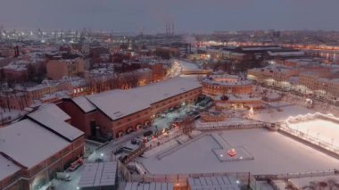 Karlı bir kış akşamında New Holland parkının hava manzarası, binaların ve sokakların gece aydınlanması, gece şehir manzarası, açık hava buz pateni pisti, arka planda St. Petersburg 'un liman vinçleri. 
