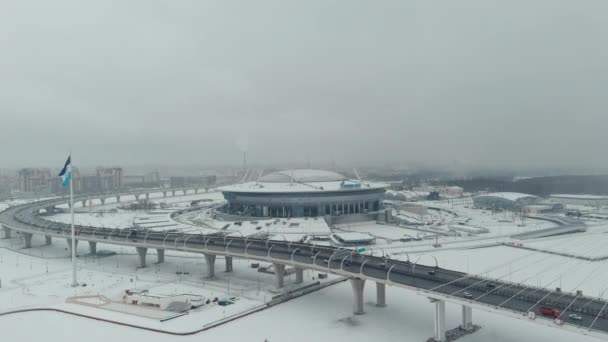 Ryssland, St Petersburg, 22 januari 2022: Drönaren flyger längs kabelbron mot den nya arenan Gazprom Arena i en snöstorm, flaggan av Zenit laget sveper på en enorm flaggstång — Stockvideo