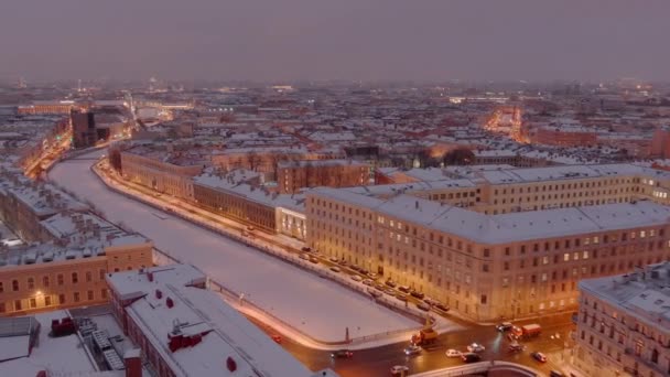 Vista aérea del terraplén del río Griboedov congelado en una noche nevada de invierno, iluminación nocturna de edificios y calles, paisaje urbano nocturno, pista de patinaje al aire libre, catedral de Isaac sobre un fondo — Vídeos de Stock