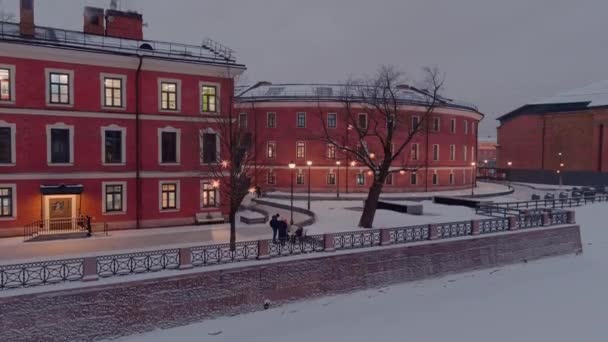 Luftaufnahme des New Holland Parks an einem verschneiten Winterabend, nächtliche Beleuchtung von Gebäuden und Straßen, nächtliches Stadtbild, Eisbahn im Freien, Sehenswürdigkeiten von St. Petersburg im Hintergrund — Stockvideo